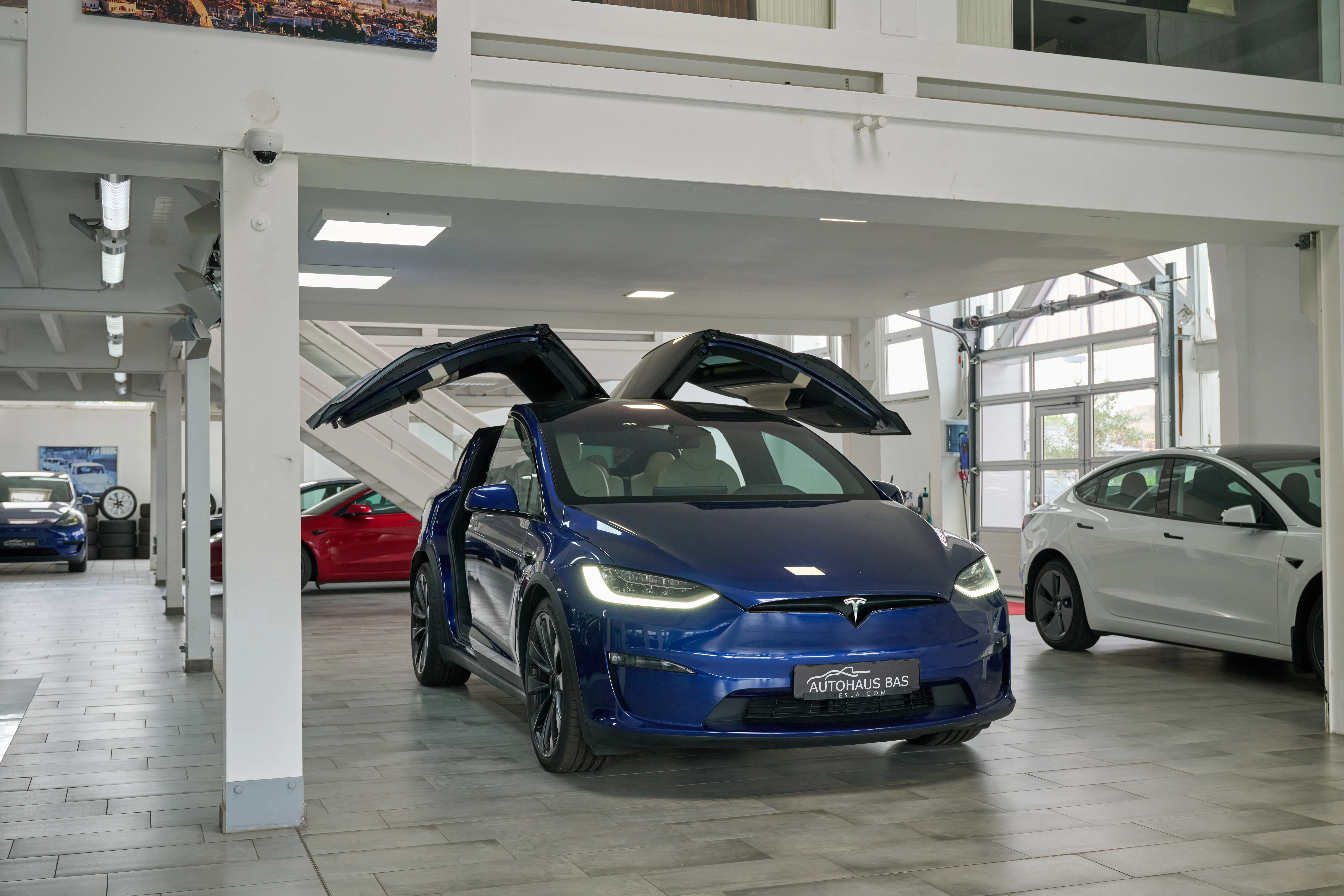 Blauer Tesla Model Y mit geöffneten Flügeltüren im Showroom des Autohaus Bas