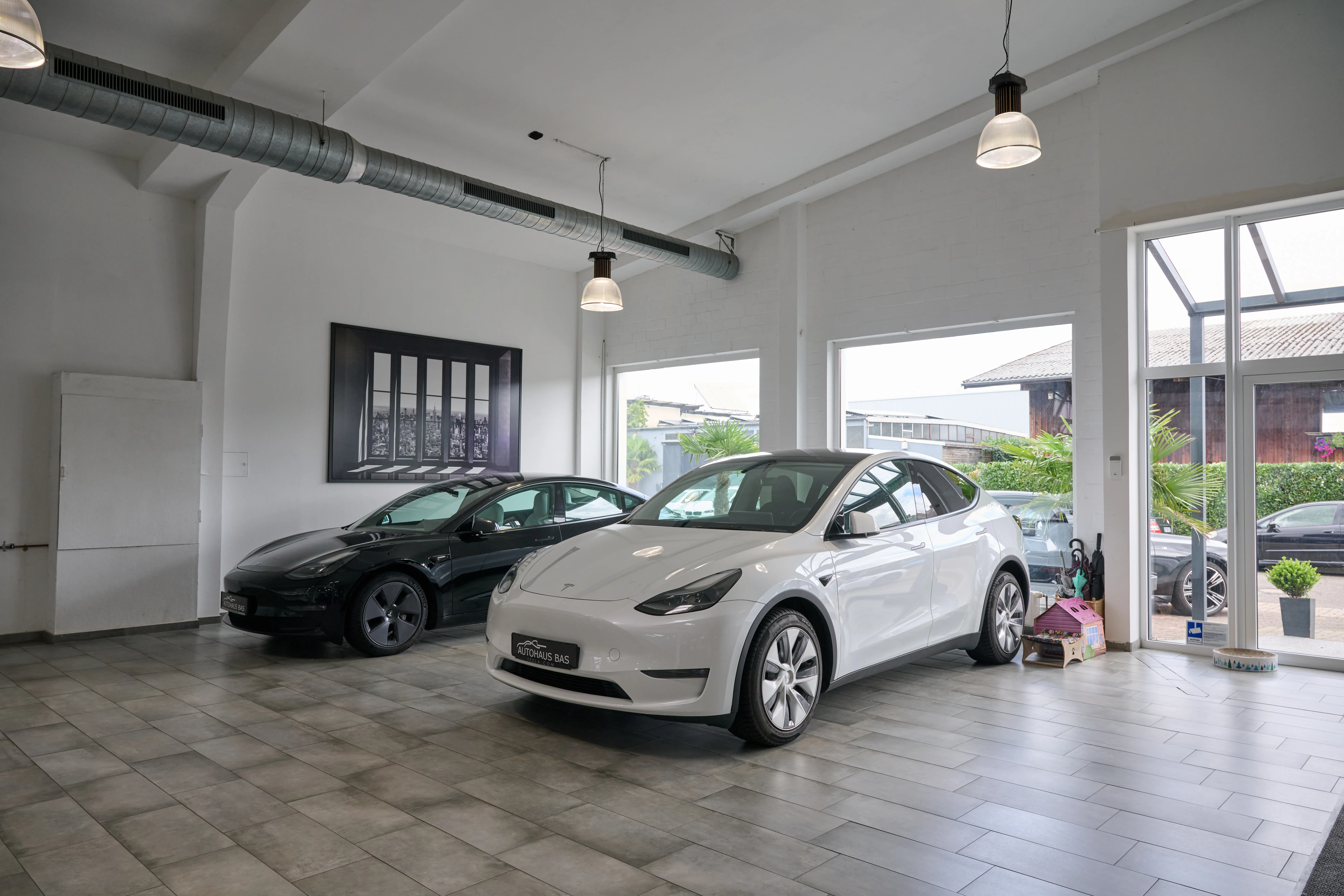 Weißer Tesla Model Y und schwarzes Model 3 im Showroom des Autohaus Bas